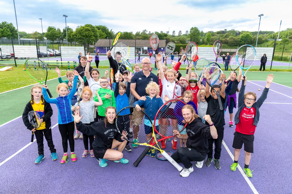 Image of the Head of BGS with children and staff of Skipton Tennis Centre - on a tennis court with rackets, cheering for the camera
