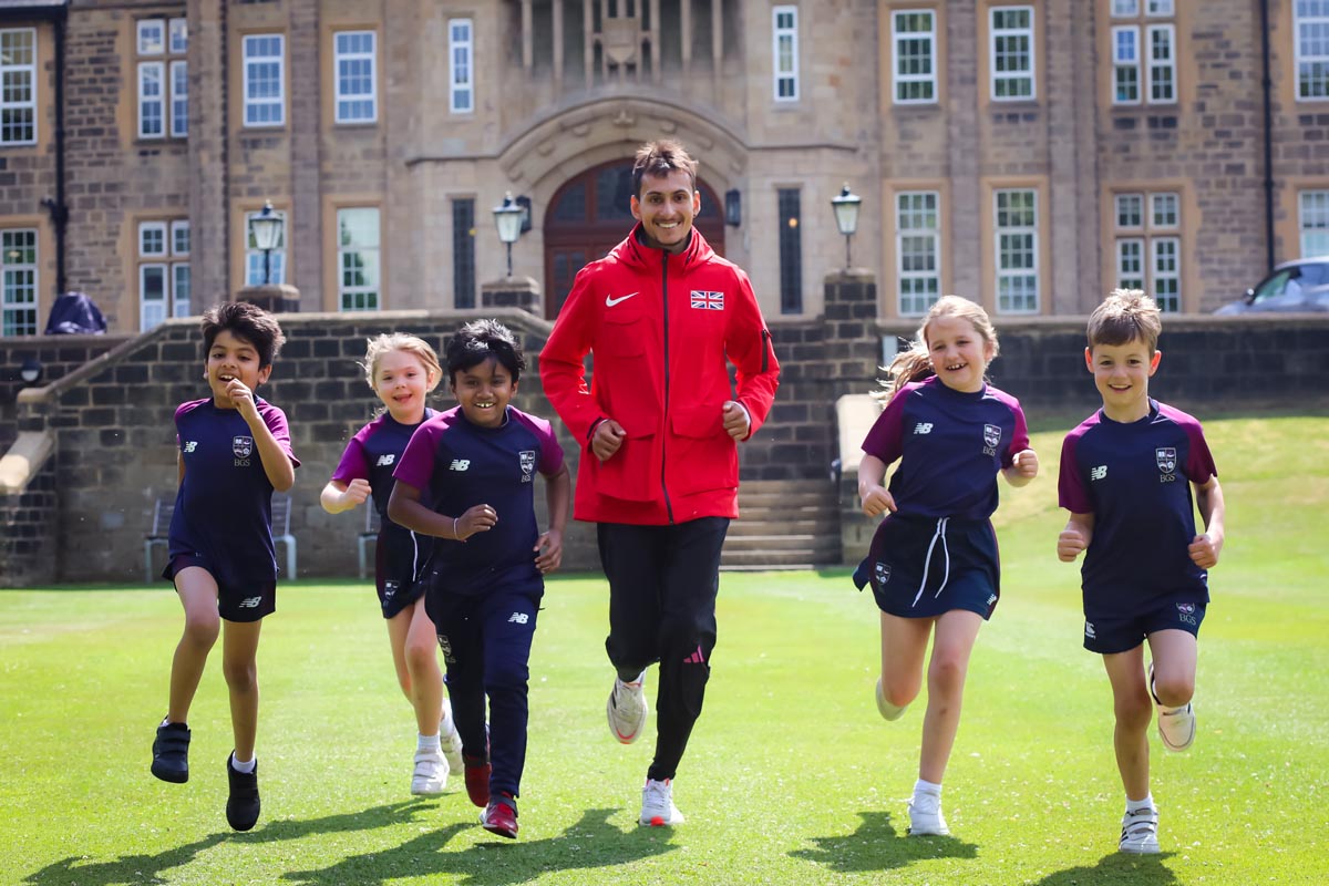 Image of one of Britain's leading athletes, Emile Cairess (centre) running outside the BGS building with five Junior School pupils