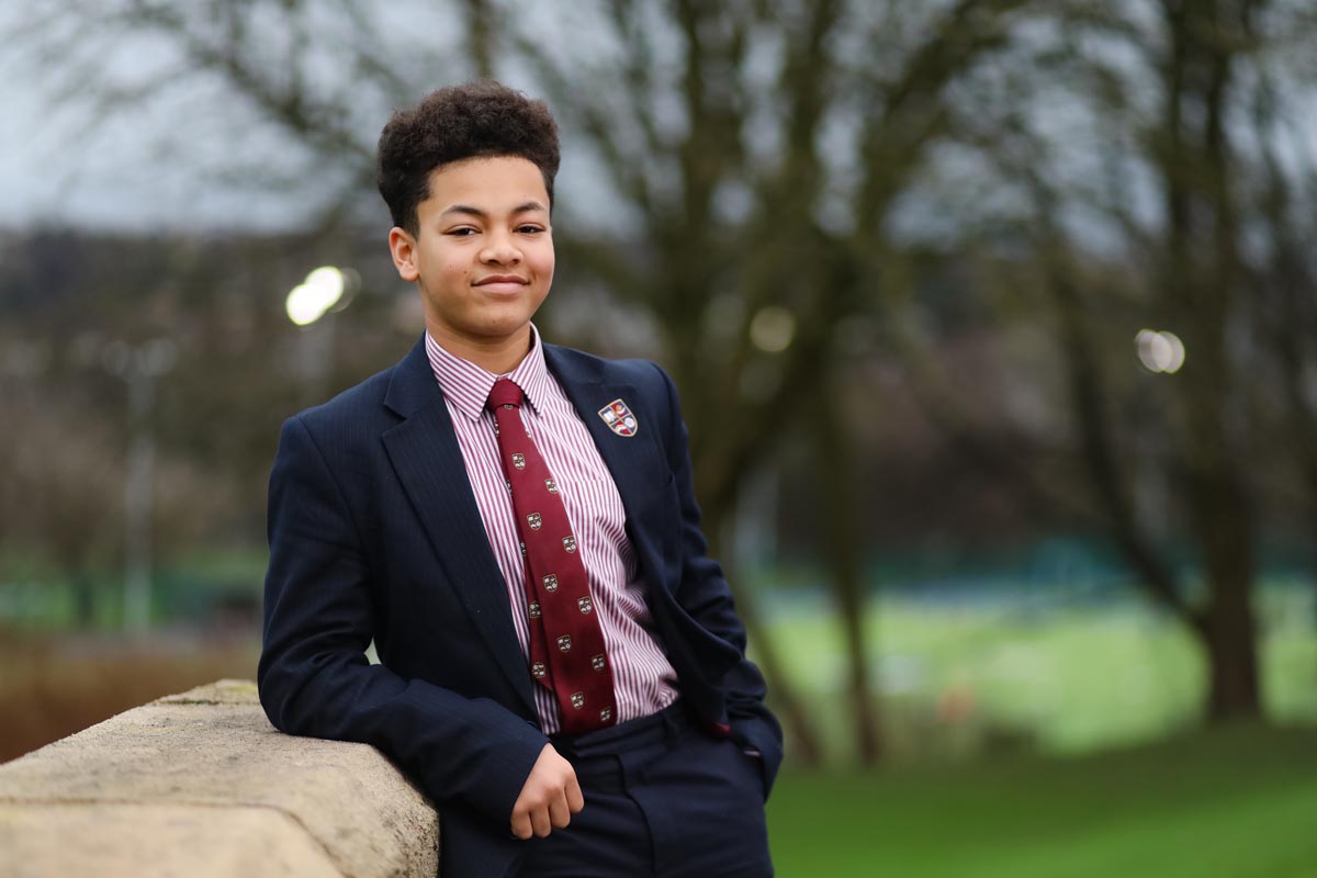 A school student in a suit and tie leaning against a wall