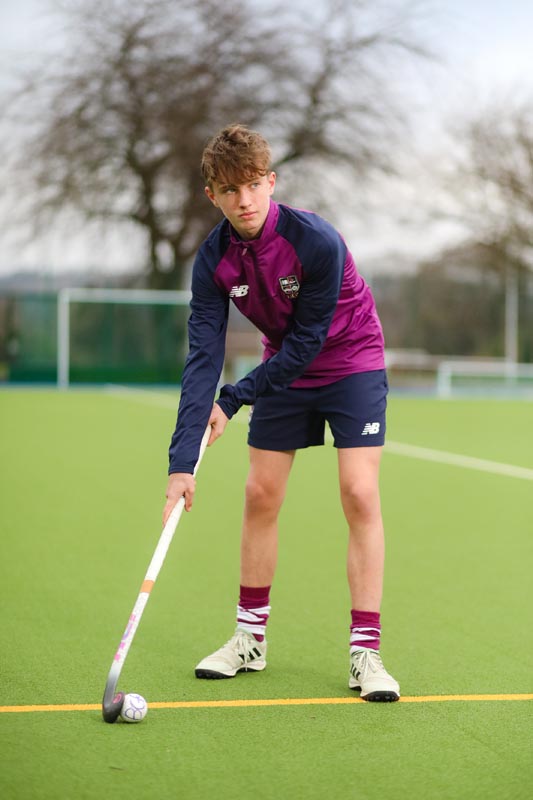 Male student hockey player on a green astro pitch with hockey stick and ball