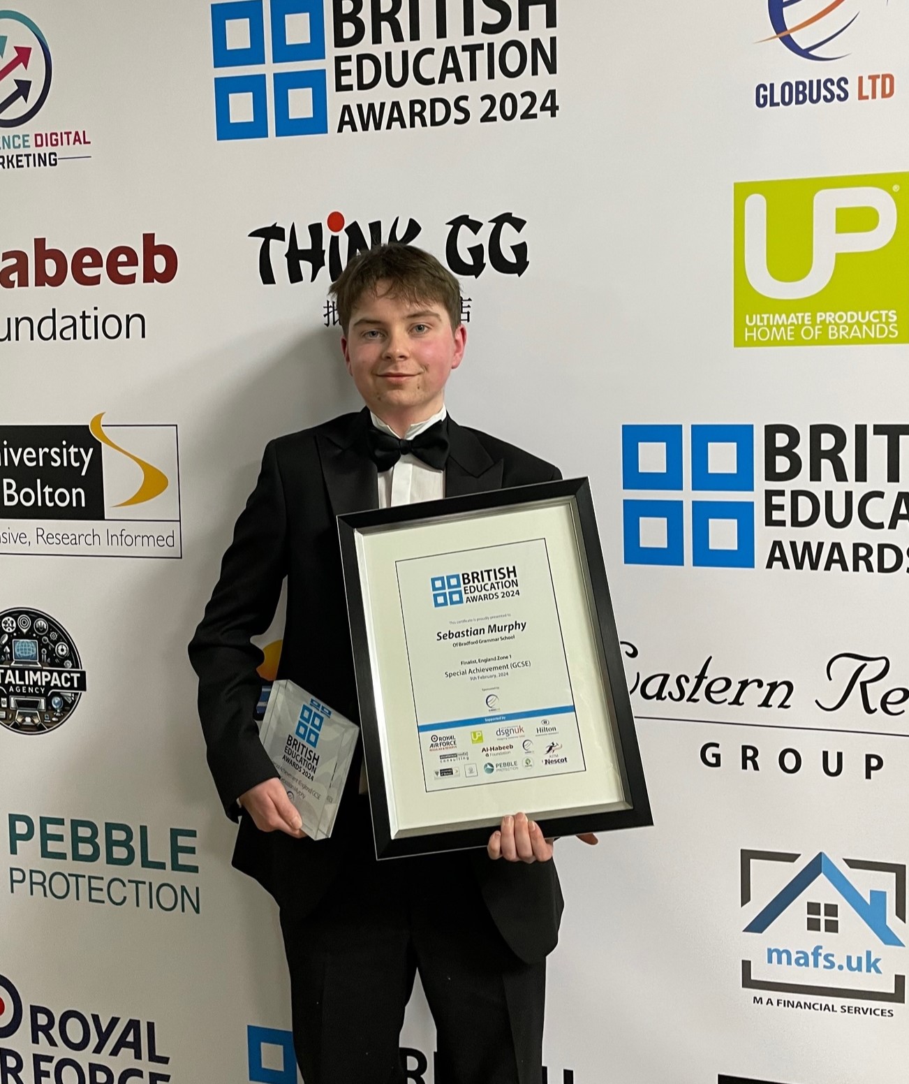 Male teenager wearing a suit and holding a certificate and award