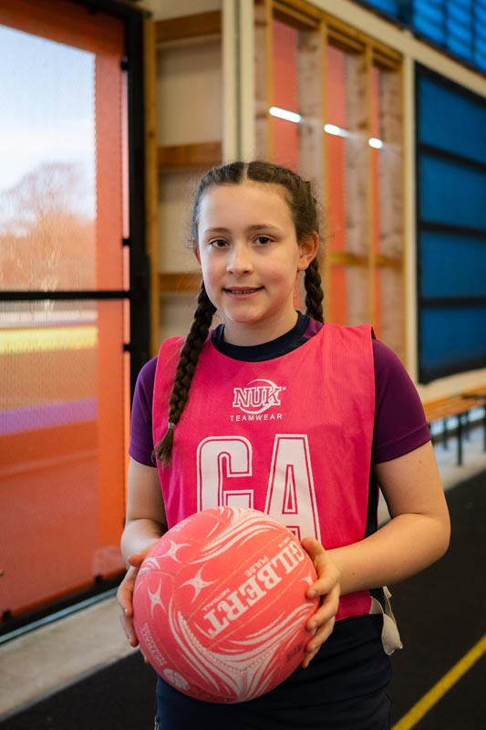 A girl in a pink GA vest holding a pink netball