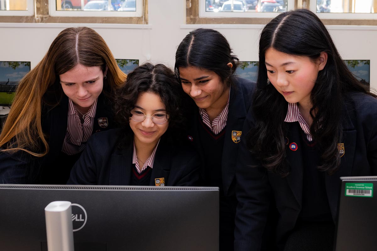 Four female pupils wearing school uniforms, attentively viewing a computer screen