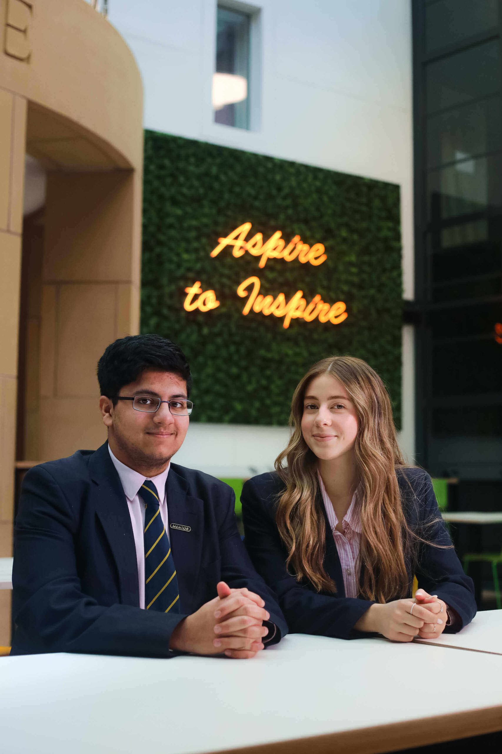 Sixth Form students sat smiling beneath the 'Aspire to Inspire' sign.