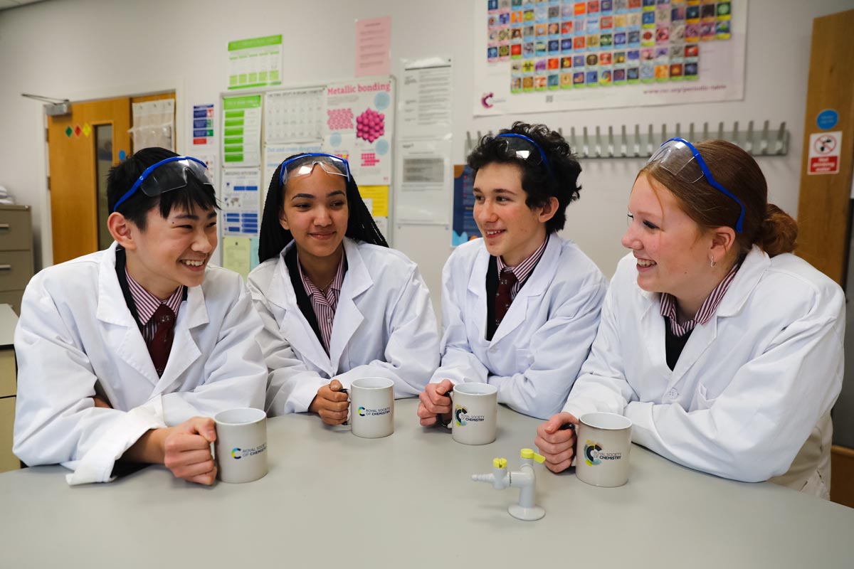 Four young smiling scientists in lab coats holding cups